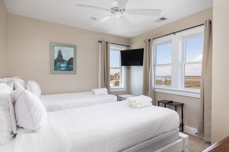 Your comfortable bedroom features two plush beds with crisp linens, ceiling fan for gentle breezes, and stunning water views through bright windows.