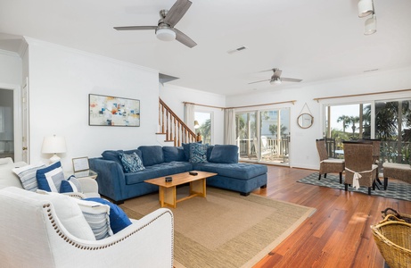 Unwind in your bright coastal living room with a plush blue sectional sofa, warm hardwood floors, and glass doors opening to your private screened porch