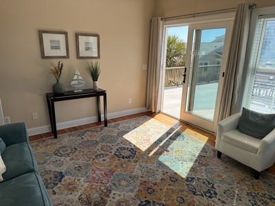 Relax in your bright living room where colorful rugs and coastal decor create a welcoming atmosphere, with sliding doors opening to your private outdoor space.