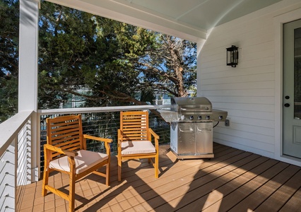 Fire up your grill on this covered deck while relaxing in modern teak chairs, surrounded by lush greenery.