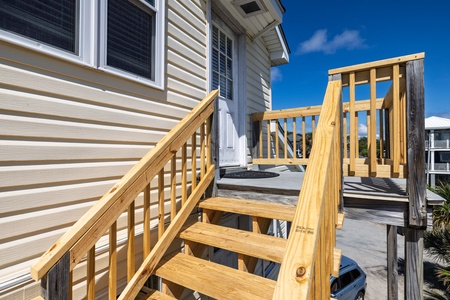 A sturdy wooden deck and stairway lead you to your private entrance, with bright blue skies overhead and the neighborhood just beyond.
