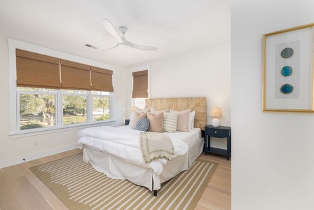 Sink into this cozy bedroom's plush bedding while natural light filters through bamboo shades, creating your perfect retreat.