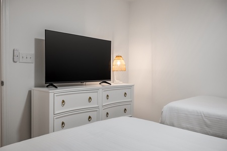 Unwind in your cozy bedroom with a large flat-screen TV and elegant white dresser. Soft lighting creates the perfect ambiance for relaxation.