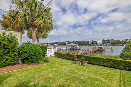Waterfront property featuring private dock access, lush landscaping with mature palm trees, manicured lawn, and serene views of the calm waterway and neighboring coastal homes.