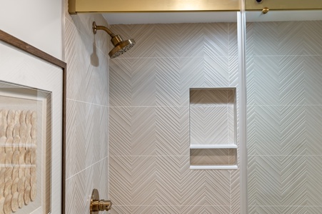 Step into your private sanctuary with elegant herringbone tile walls, brass fixtures, and built-in storage niches for all your essentials.