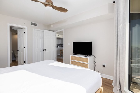 Rest in your bright bedroom with crisp linens, ceiling fan, and modern TV setup for ultimate comfort.
