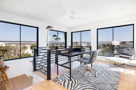 Your stylish workspace awaits with panoramic windows flooding natural light across the zebra-print rug and sleek modern desk.