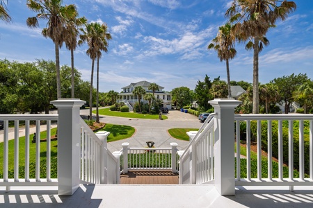 A grand entrance framed by towering palms and lush landscaping welcomes you to this coastal retreat. The majestic main house sits nestled among mature trees, offering a serene arrival experience in this exclusive waterfront community.