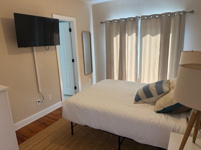 Sink into crisp white linens in your peaceful bedroom, where warm natural light filters through elegant curtains and modern amenities await.