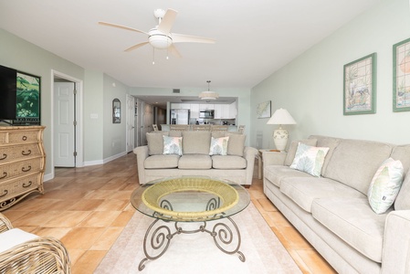 Relax in your spacious living room with plush sofas, ceiling fan, and open kitchen - perfect for unwinding after beach days.