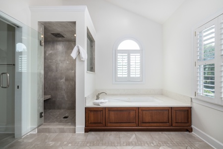 Unwind in your elegant bathroom sanctuary featuring a soaking tub framed by rich wood cabinetry and bright plantation shutters, with a luxurious walk-in shower just steps away.