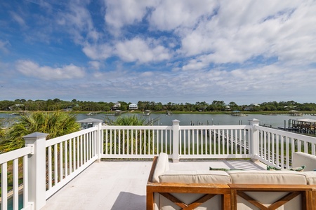 A spacious waterfront deck overlooks calm waters and lush coastal scenery under sweeping blue skies and dramatic clouds—an idyllic setting defining the character of this coastal property and its natural surroundings.