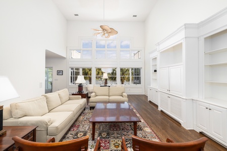 Relax in your spacious living room with soaring ceilings, elegant built-ins, and sunlight streaming through transom windows overlooking swaying palms.
