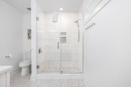 Step into your private spa-like retreat, where calming white tones, elegant textured tiles, and a spacious glass-enclosed shower invite you to unwind completely.