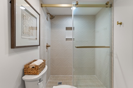 Step into your elegant bathroom featuring a spacious glass-enclosed shower with beautiful herringbone tile work and warm brass accents.