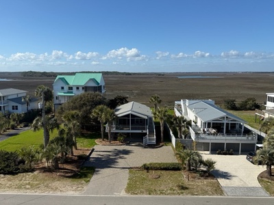 Coastal properties sit along a quiet residential area with expansive marsh views stretching toward the horizon under clear blue skies.