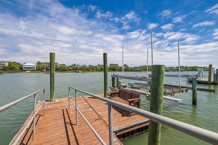 Private boat dock with bench seating overlooks calm waterway, framed by coastal vegetation and blue skies, offering direct water access for your boating adventures.