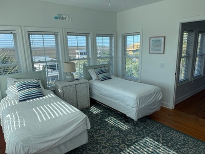 Wake up in this bright twin bedroom with stunning water views streaming through floor-to-ceiling windows, creating peaceful morning light patterns.