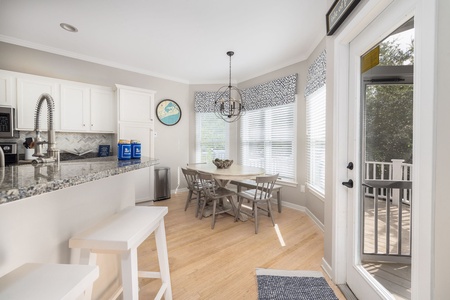Sunlit breakfast nook with bay windows, seating for six, and chic coastal chandelier