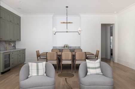 Your open-concept living space blends dining and relaxation with sage cabinetry, cozy armchairs, and warm wood floors perfect for gathering.