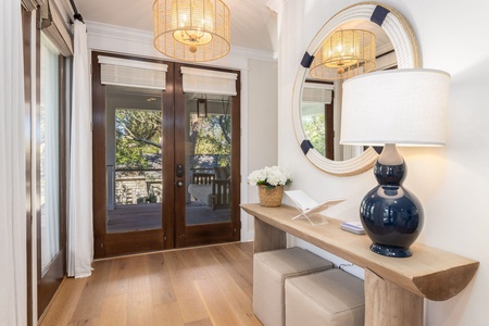 Step into your elegant entryway where warm wood fixtures cast a welcoming glow over polished hardwood floors and thoughtful coastal touches