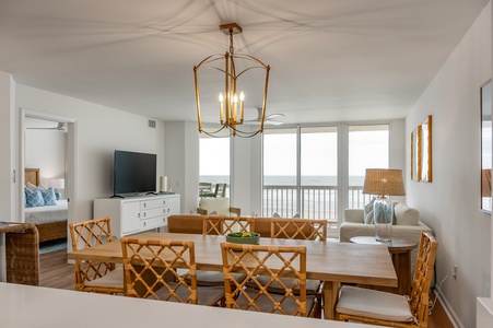 Your elegant dining space features coastal charm with bamboo chairs and sweeping ocean views through floor-to-ceiling windows.