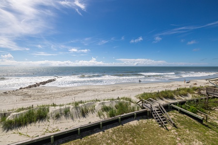 Steps from this property lead directly to a pristine sandy beach where gentle waves lap the shore and endless coastal views stretch across the horizon under brilliant blue skies.