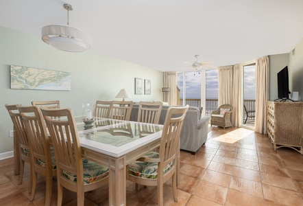 Your bright oceanfront living and dining space flows seamlessly together, featuring coastal-inspired furnishings and sweeping water views through floor-to-ceiling windows.