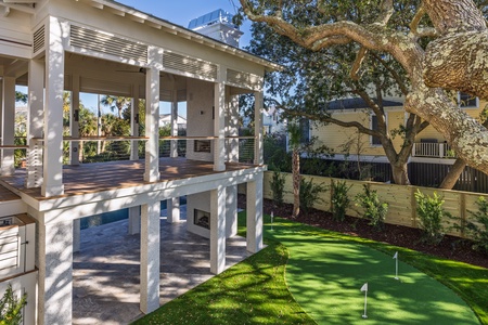 Modern vacation home featuring a putting green and covered outdoor entertaining spaces surrounded by mature trees.