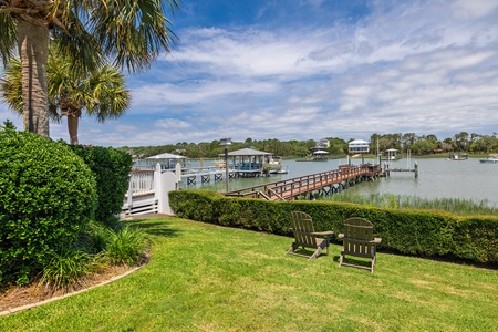 The property features a tranquil waterfront location with a private dock and boardwalk extending over calm waters, surrounded by lush coastal landscaping and neighboring homes.