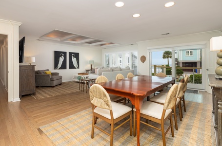 Your spacious open-concept living and dining area features warm wood floors, comfortable seating, and coastal artwork that sets a relaxing beach house mood.