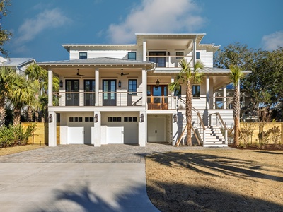 Modern coastal architecture featuring expansive covered porches and palm-lined driveway creates an impressive arrival experience.