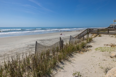 Pristine beach with soft sand, rolling waves, and wooden boardwalk access just steps from the property.