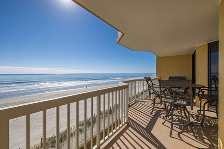 Oceanfront balcony with dining table and chairs overlooking pristine beach and endless blue waters.