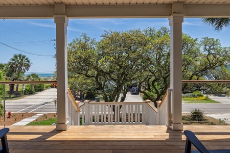 Covered porch overlooking a tree-lined street with distant glimpses of the coastline, providing a peaceful arrival experience.