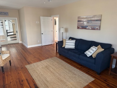 Unwind on the plush navy sofa with striped cushions, surrounded by warm wood floors and coastal artwork that creates your perfect retreat.
