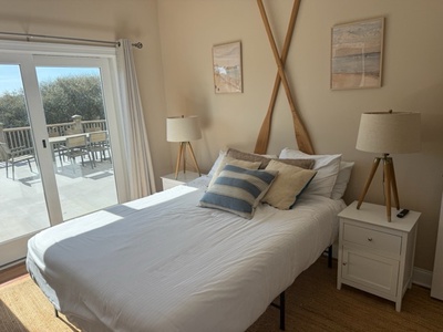 Wake up to sunshine streaming through your private terrace doors in this serene bedroom with coastal-inspired decor and tripod lamps.