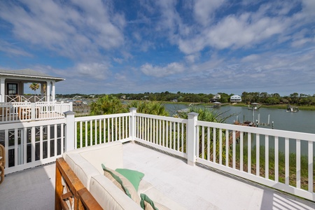 Expansive waterfront terrace captures peaceful coastal living with scenic views of winding waterways, marshlands, and neighboring homes nestled along the shoreline.