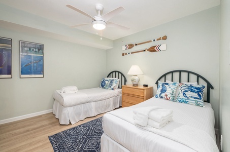 Relax in your coastal-themed twin bedroom with crisp linens, decorative oars, and a cooling ceiling fan for peaceful nights.