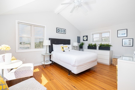 Sink into crisp white linens and let the overhead fan keep you cool as natural light pours through large windows. The warm wood floors and pops of greenery create a serene retreat where you'll sleep soundly.