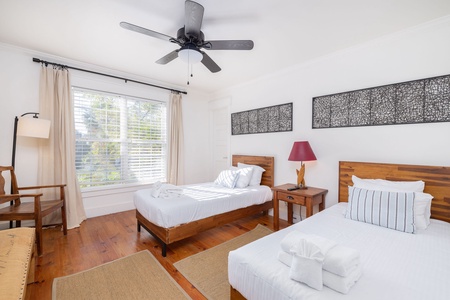 Bright guest bedroom with twin beds, coastal artwork, and plenty of natural light — perfect for kids or friends traveling together.