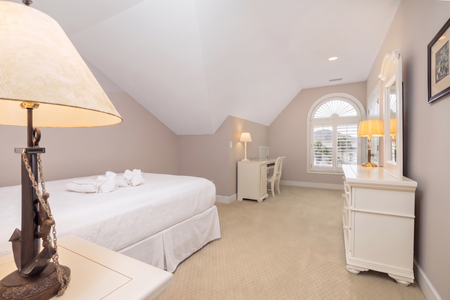 Slip into crisp white linens and let the soft glow of elegant lamps lull you into deep relaxation. This serene bedroom offers plush bedding, a cozy workspace by the window, and a peaceful ambiance perfect for your restful retreat.