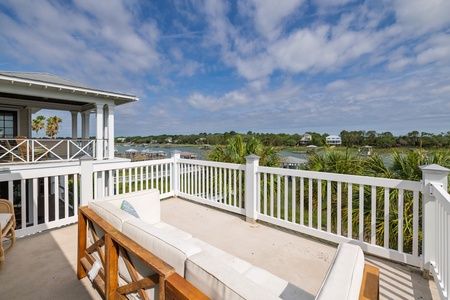 Stunning waterfront deck framed by elegant white railings and lush palms. Lounge here with waterfront breezes and sweeping views across the peaceful river to distant homes.