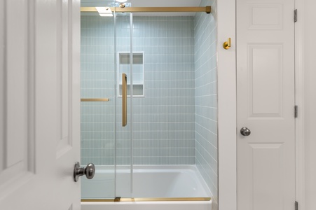 Step into your private spa-like shower featuring elegant glass doors, soothing blue tile, and warm brass accents for pure relaxation.