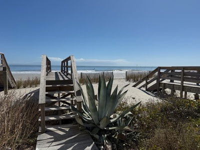 Wooden boardwalk leading to pristine sandy beach with clear blue skies and ocean views.