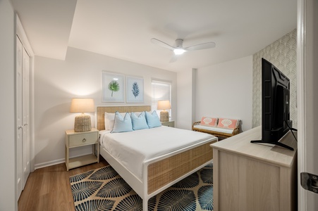 Unwind in your coastal-inspired bedroom featuring a plush queen bed, tropical artwork, and modern amenities for the perfect beachside retreat.