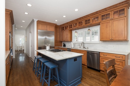 Your gourmet kitchen features warm wood cabinetry, marble countertops, stainless steel appliances, and a central island with seating—perfect for preparing meals and gathering together.