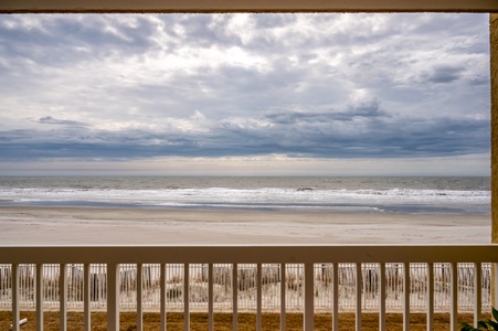 Unobstructed oceanfront views showcase pristine sandy shores and rolling waves beneath dramatic cloudy skies from this beachside property.