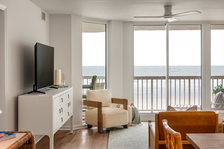Relax in your bright oceanfront living room with stunning sea views through floor-to-ceiling windows and modern coastal furnishings.
