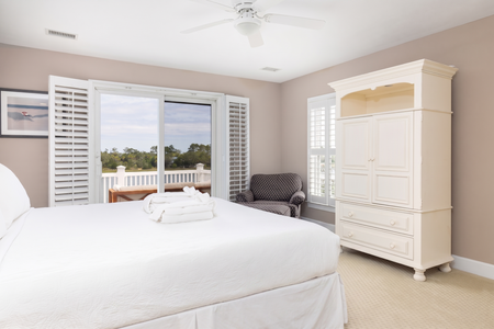 Wake up to natural light and serene views framed by plantation shutters. Your private balcony invites you to savor morning coffee overlooking peaceful surroundings while the plush bedding and cozy armchair promise complete relaxation.